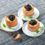 Cáscaras de huevo rellenas de crema y caviar negro con cuchara de cobre — fotografía gastronómica Barcelona